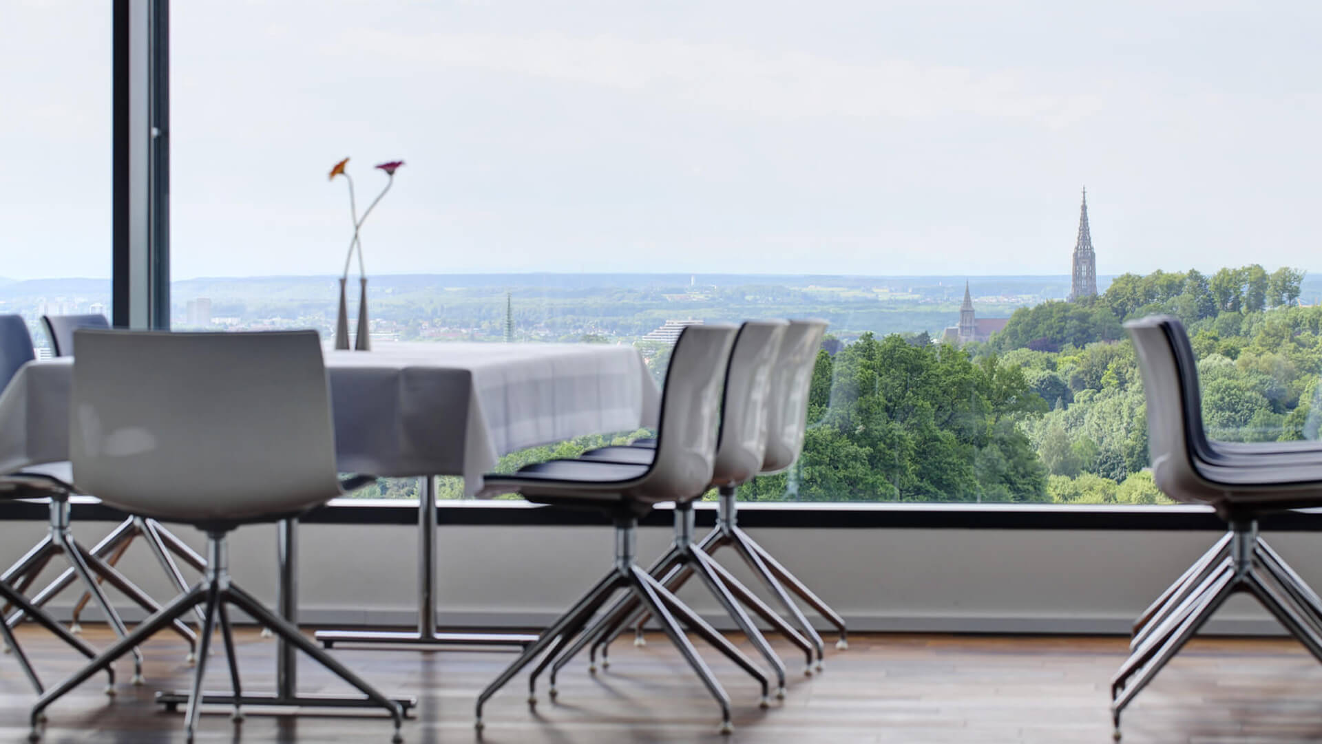 Tisch mit Stühlen und großer Fensterfront, die das Ulmer Münster im Hintergrund zeigt